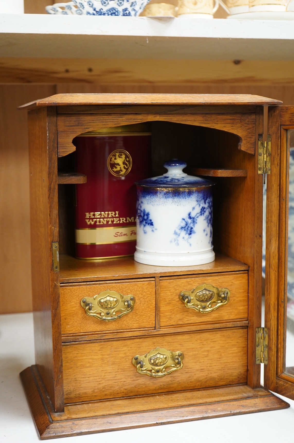An Edwardian oak smoker's cabinet, with Doric blue and white tobacco jar and cover, 38cm high x 29.5cm wide.